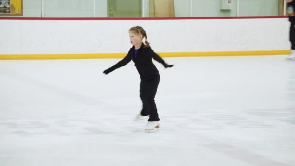 Kleines Mädchen übt Eiskunstlauf auf einer überdachten Eisbahn.
