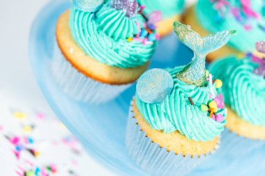 Üzerinde mavi tereyağlı krema süslemesi ve çikolata denizkızı kuyruğu ile süslenmiş gurme deniz kızı kekleri..