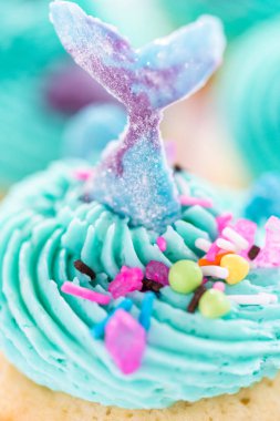 Üzerinde mavi tereyağlı krema süslemesi ve çikolata denizkızı kuyruğu ile süslenmiş gurme deniz kızı kekleri..