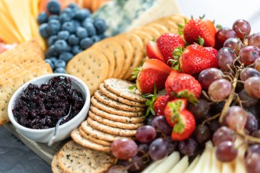 Aperatif olarak sunulan tahtanın üzerinde gurme peyniri, kraker ve meyve var..