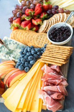 Aperatif olarak sunulan tahtanın üzerinde gurme peyniri, kraker ve meyve var..