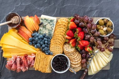 Düz yatıyordu. Aperatif olarak sunulan tahtanın üzerinde gurme peyniri, kraker ve meyve var..