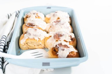 Taze pişmiş tarçınlı rulo, beyaz kremalı, mavi bir tavada..