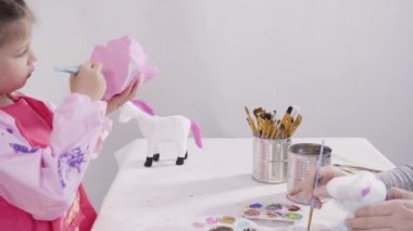 Düz yatıyordu. Küçük kız evde eğitim projesi için akrilik boyayla heykelcikler boyuyor..