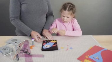 Anne çocuklara el sanatları masasında dikiş setiyle dikiş dikmeyi öğretiyor..