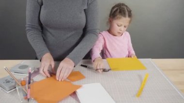 Anne çocuklara el sanatları masasında dikiş setiyle dikiş dikmeyi öğretiyor..