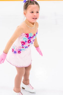 Güzel pembe elbiseli, çiçekli küçük bir kız buz pateni pistinde artistik patinaj yapıyor..
