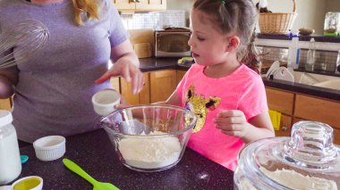 Küçük kız annesiyle mutfakta yassı ekmek pişiriyor..