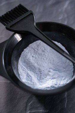 Siyah arka planda siyah plastik bir kasede saç boyası tozu..
