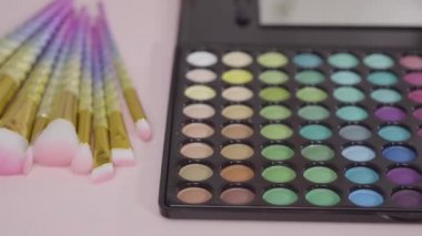 Beyaz arka planda tek boynuzlu at temalı makyaj fırçaları ve göz falı paleti.