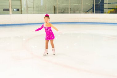 Pembe elbiseli küçük artistik patinajcı kapalı buz pistinde pratik yapıyor..