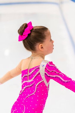 Pembe elbiseli küçük artistik patinajcı kapalı buz pistinde pratik yapıyor..
