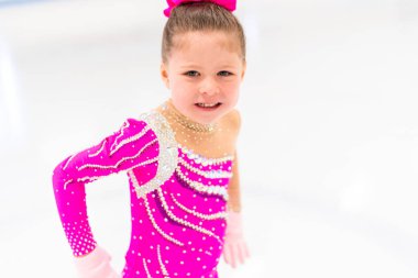 Pembe elbiseli küçük artistik patinajcı kapalı buz pistinde pratik yapıyor..