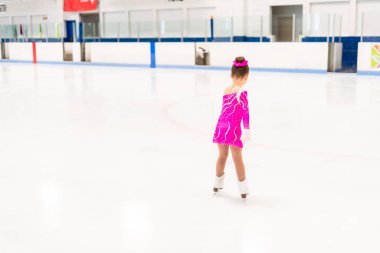 Pembe elbiseli küçük artistik patinajcı kapalı buz pistinde pratik yapıyor..