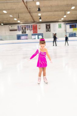 Pembe elbiseli küçük artistik patinajcı kapalı buz pistinde pratik yapıyor..