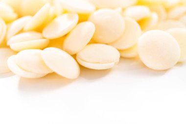 Beyaz arka planda çikolata şekillerini eritmek için beyaz yuvarlak çikolata parçaları..