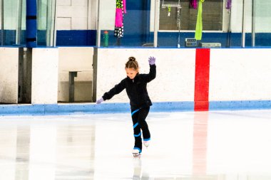 Siyah elbiseli küçük artistik patinajcı, kapalı buz arenasında pratik yapıyor..