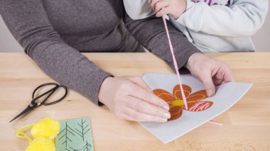 Küçük kız annesiyle el sanatları masasında dikiş dikmeyi öğreniyor..