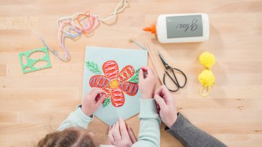 Küçük kız annesiyle el sanatları masasında dikiş dikmeyi öğreniyor..