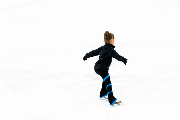 穿着黑色衣服的小花样滑冰选手在室内冰场上练习 — 图库照片