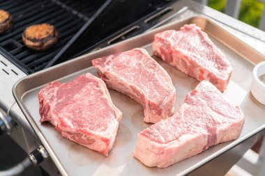 Çiğ New York bifteği tepside ızgarada kızarmaya hazır..