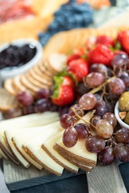 Aperatif olarak sunulan tahtanın üzerinde gurme peyniri, kraker ve meyve var..