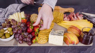 Arranging gourmet cheese, crakers, and fruits on a board for a large cheese board. clipart