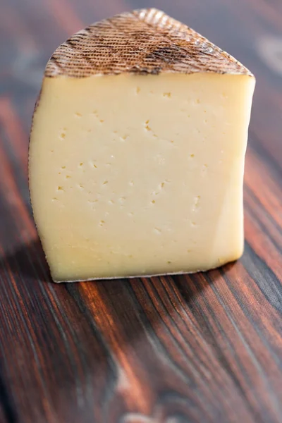 濃い木の背景に熟成したマンチェゴチーズの大きなくさび — ストック写真