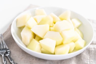 Beyaz bir kasede dilimlenmiş altın çiğ taneli kavun..