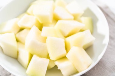 Beyaz bir kasede dilimlenmiş altın çiğ taneli kavun..