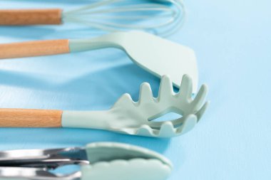 Mavi arka planda ahşap saplı yeni mavi silikon mutfak aletleri..