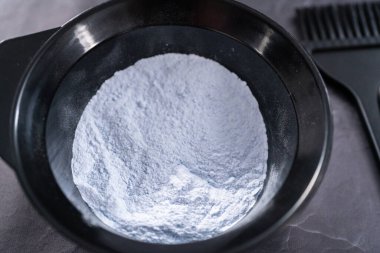 Siyah arka planda siyah plastik bir kasede saç boyası tozu..