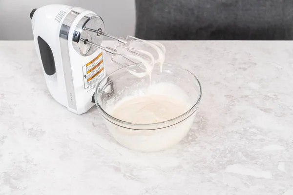 Mixing ingredients in a glass mixing bowl to prepare cream cheese frosting.