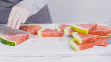 Kırmızı karpuzu beyaz bir kesme tahtasının üzerinde küçük parçalara ayırmak.