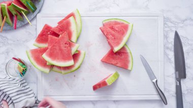 Düz yatıyordu. Kırmızı karpuzu beyaz bir kesme tahtasının üzerinde küçük parçalara ayırmak.