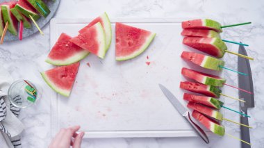 Düz yatıyordu. Kırmızı karpuzu beyaz bir kesme tahtasının üzerinde küçük parçalara ayırmak.