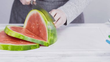 Kırmızı karpuzu beyaz bir kesme tahtasının üzerinde küçük parçalara ayırmak.