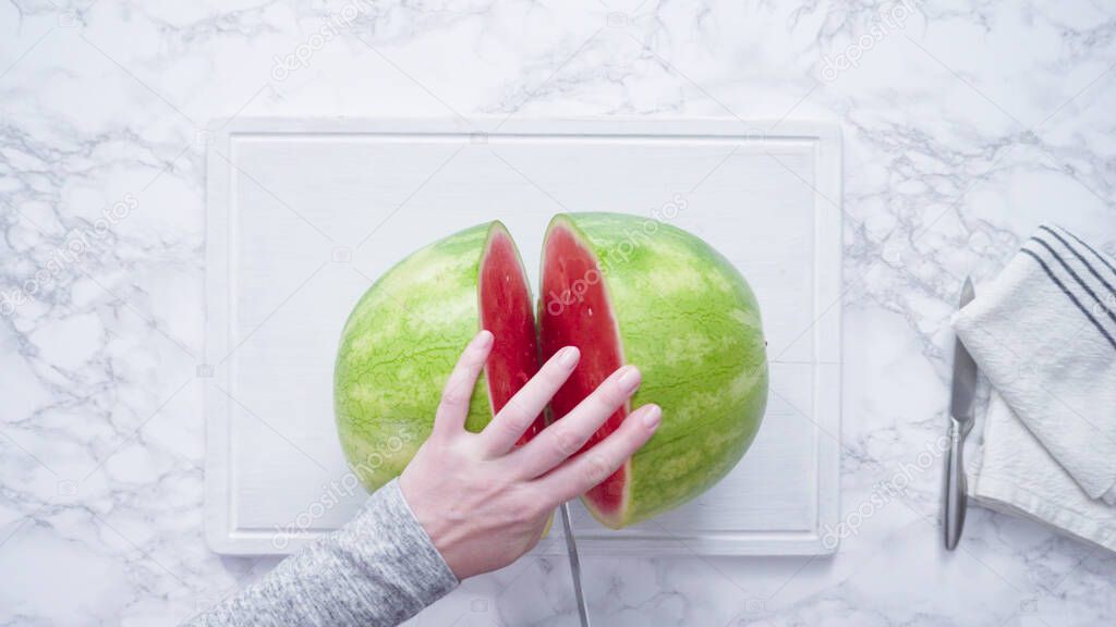Flat lay. Slicing red watermelon into small pieces on a white cutting board.