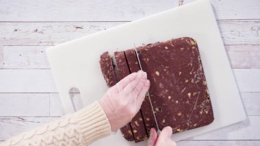 Düz yatıyordu. Adım adım. Beyaz kesim tahtasında ev yapımı macadamia şekerlemesi kesiyorum..