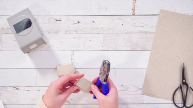 Düz yatıyordu. Adım adım. Kahverengi kağıttan hediye etiketlerini kağıt punçla kesiyor..