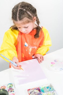 Evde akrilik boyalı bir sanat projesi üzerinde çalışan küçük bir kız..