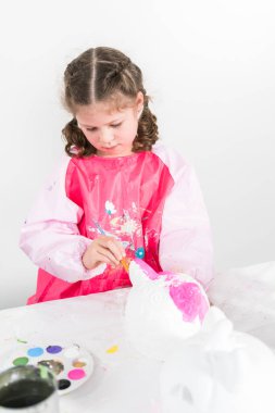 Küçük kız Cadılar Bayramı balkabağını akrilik boyayla boyuyor.