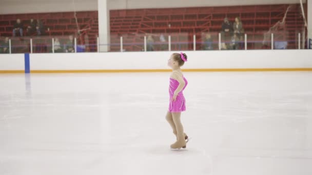 小さな女の子でA可愛いですピンクドレスともに花練習フィギュアスケートムーブオンザ屋内アイスリンク — ストック動画