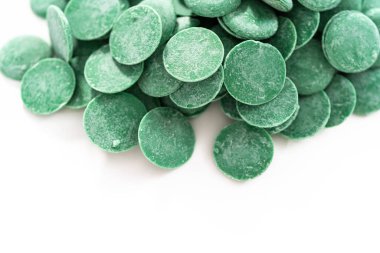 Beyaz arka planda çikolata şekillerini eritmek için yeşil yuvarlak çikolata parçaları..