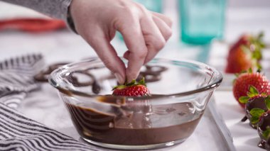 Adım adım. Çikolata kaplı çilek hazırlamak için organik çilekleri erimiş çikolatayla bir kaseye daldırmak..