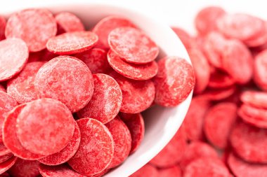 Beyaz arka planda çikolata şekillerini eritmek için kırmızı yuvarlak çikolata parçaları..