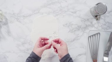 Mermer tezgahın üzerindeki beyaz fondanla kar tanelerini keserek..