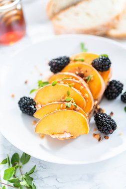 Beyaz tabakta böğürtlenlerle süslenmiş şeftalili ricotta tostu.