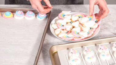 Adım adım. Taze pişmiş tek boynuzlu at kurabiyelerini fırından alıp beyaz servis tabağına koyuyorlar..