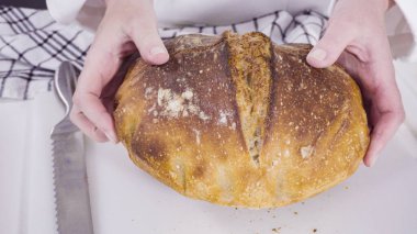 Beyaz bir kesme tahtasının üzerinde taze ekşi ekmek dilimliyorum..